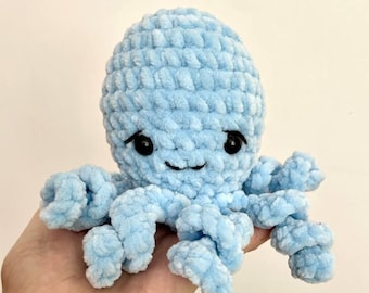 May include: A light blue crocheted octopus with black eyes and a smiling mouth. The plush toy has eight curled tentacles and a textured, fluffy appearance. The octopus is a handmade item.