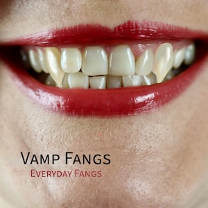 May include: Close-up of a person's mouth with red lipstick and two prominent, pointed, white teeth, commonly known as fangs. The text "VAMP FANGS EVERYDAY FANGS" is below the mouth.