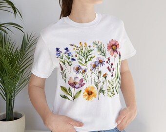 Op de afbeelding: Wit T-shirt met een aquarel bloemenprint met verschillende bloemen in tinten roze, paars, geel en blauw.