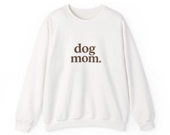 May include: A white crewneck sweatshirt with the text "dog mom." in brown lettering. The sweatshirt has long sleeves and a classic, casual design, perfect for dog lovers.