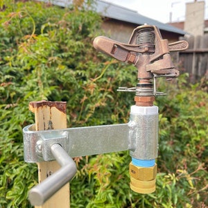 May include: A brass sprinkler head with a metal bracket and a blue and gold connector. The sprinkler head is attached to a metal pole.
