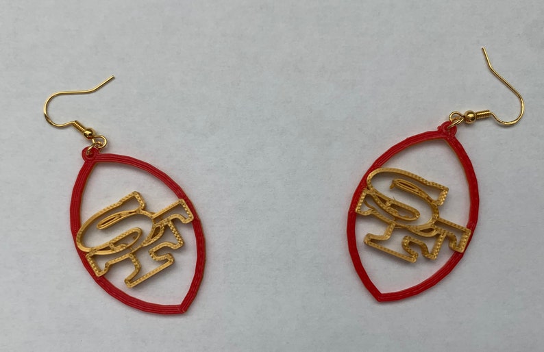 May include: A pair of red and gold earrings shaped like a football with the letters "SF" inside.
