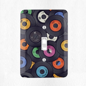 May include: A light switch cover featuring a collage of vintage vinyl records with colorful labels. The records are arranged in a random pattern, creating a visually appealing and nostalgic design.