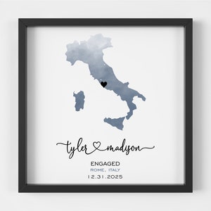 May include: A watercolor illustration of Italy with a black heart marking the location of Rome. The text below reads "Tyler & Madison Engaged Rome, Italy 12.31.2025".
