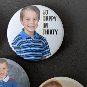 May include: Two round buttons with photos of children and text. The first button has a photo of a young boy wearing a blue and white striped shirt. The text reads "SO HAPPY IM THIRTY". The second button has a photo of a young girl wearing a yellow hoodie and glasses. The text reads "IN MY THIRTIES ERA".