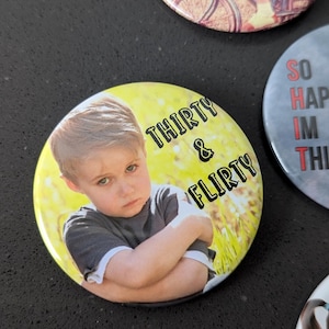 May include: A yellow button with a photo of a young boy with a serious expression. The text "THIRTY & FLIRTY" is printed in black on the button.