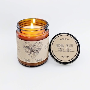 May include: A brown glass candle jar with a label that says "John + Sarah" and a map of Las Vegas in the shape of a heart. The lid of the jar has a label that says "Burning Bright Since 2016".