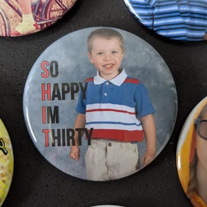 May include: Four round buttons with photos of children and text. The first button shows a child riding a bicycle. The second button shows a child wearing a blue and white striped shirt with the text "SO HAPPY I'M THIRTY". The third button shows a child wearing a blue and white striped shirt. The fourth button shows a child with pigtails wearing a blue and white shirt with the text "I AM SO".