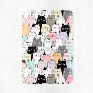 May include: A light switch cover with a colorful pattern of cartoon cats. The cats are in various colors, including pink, blue, green, yellow, and gray. The cats have different expressions, some are smiling, some are looking straight ahead, and some are looking to the side.