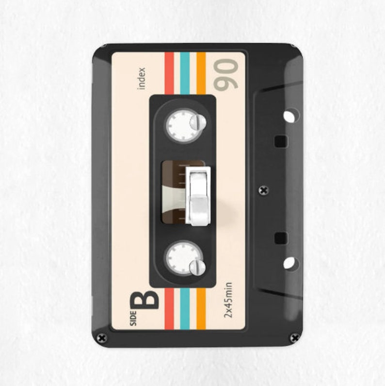 May include: A black cassette tape light switch with a white toggle switch. The cassette tape has a white label with the text "index" and "90" printed on it. The cassette tape also has the text "SIDE B" and "2x45min" printed on it. The cassette tape has a colorful stripe design.