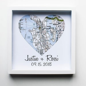 May include: A white framed print with a heart-shaped map of Seattle, Washington. The map is in black and white with blue water features. The text "Justin & Rossi 09.15.2018" is printed below the map.