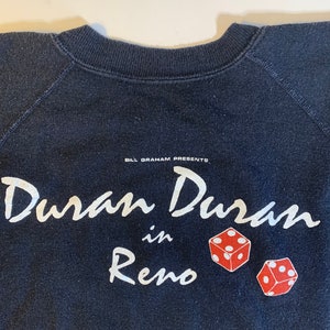 May include: Black sweatshirt with white text that reads "Bill Graham Presents: Duran Duran in Reno" with two red dice printed below the text.