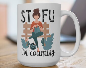 Puede incluir: Taza de cerámica blanca con una ilustración en blanco y negro de una persona tejiendo en un banco. El texto "STFU I'm counting" está impreso en la taza.