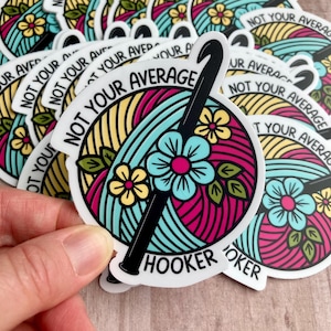 A colorful floral sticker with the words "not your average hooker" and a crochet hook. The main colors are magenta, green, yellow, and aqua.