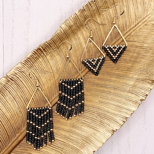 May include: Two pairs of drop earrings featuring gold-toned triangular frames. Each earring is adorned with a geometric pattern of small black and gold beads, with the larger pair featuring a fringe of hanging black and gold beaded strands.