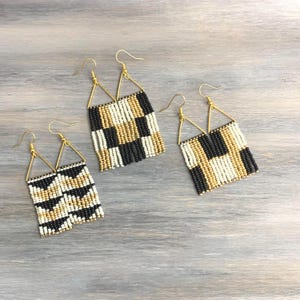 May include: Three pairs of dangle earrings crafted from small black, white, and gold beads. Each earring features a triangular gold-tone wire hook attached to a rectangular beaded panel with geometric patterns, including checkered and chevron designs.