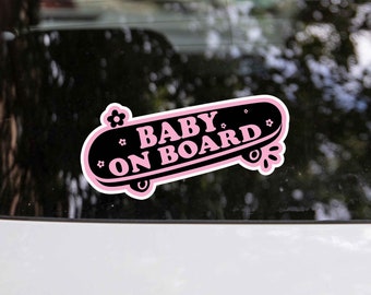 May include: Pink and black car sticker with a skateboard design that says "Baby on Board".