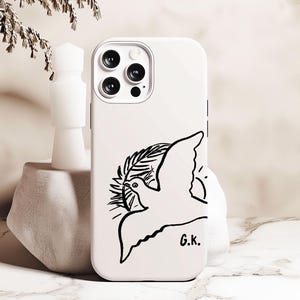 May include: White phone case with a black line drawing of a dove with an olive branch in its beak. The dove is flying towards the sun. The text "G.K." is printed in the bottom right corner.