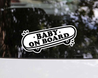May include: A white sticker with black text that says "Baby on Board" on a skateboard design. The sticker is on the back window of a car.