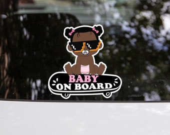 May include: A black and white car sticker with a cartoon illustration of a baby wearing sunglasses and a pink nappy, riding a skateboard. The text "BABY ON BOARD" is written in pink letters on the skateboard.