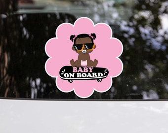 May include: Pink flower-shaped car sticker with a cartoon baby girl wearing sunglasses and a dummy, riding a skateboard. The text "BABY ON BOARD" is written in black letters on the skateboard.