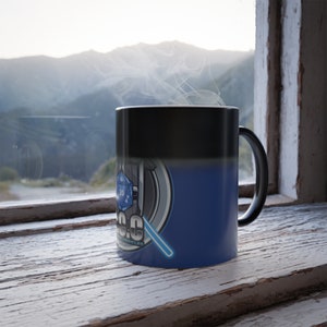 May include: A black and blue color-changing mug with a graphic of a 20-sided die and a lightsaber. The text "D&D Chronicles" is on the mug.
