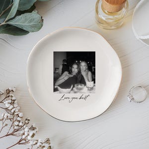 Peut inclure: Un vide-poche en c&eacute;ramique blanche avec un bord dor&eacute; pr&eacute;sente une photo en noir et blanc de deux personnes. Les mots "Love you best" sont &eacute;crits en dessous de la photo en cursive. Une bague et une petite bouteille sont &eacute;galement visibles.