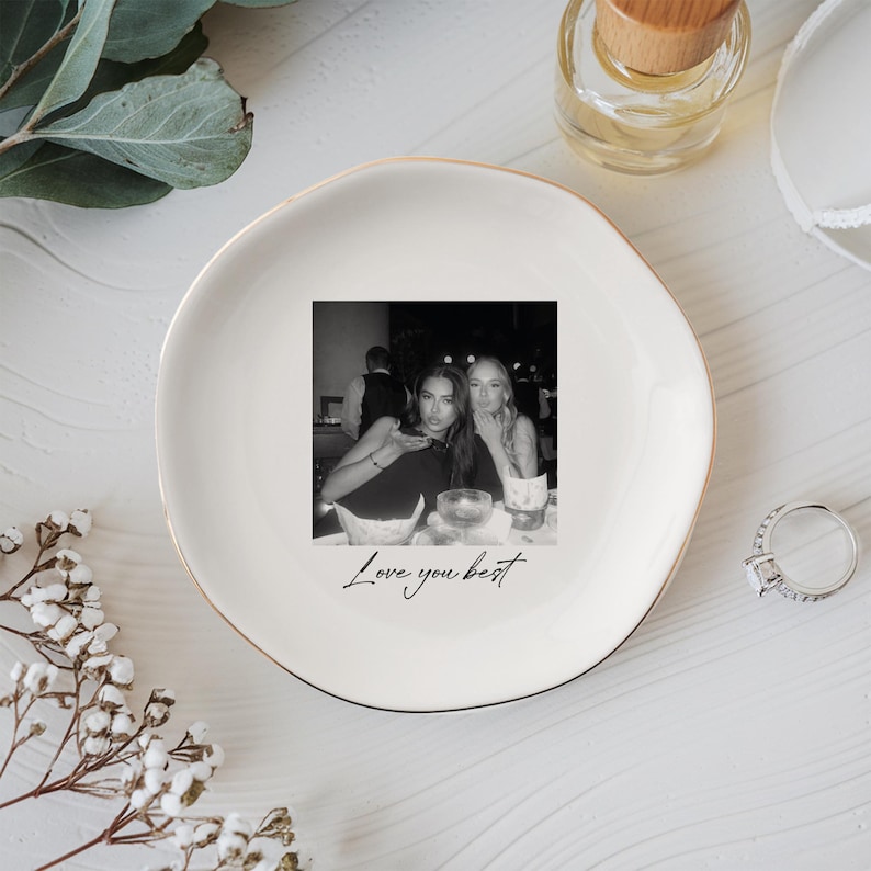 Peut inclure: Un vide-poche en c&eacute;ramique blanche avec un bord dor&eacute; pr&eacute;sente une photo en noir et blanc de deux personnes. Les mots "Love you best" sont &eacute;crits en dessous de la photo en cursive. Une bague et une petite bouteille sont &eacute;galement visibles.