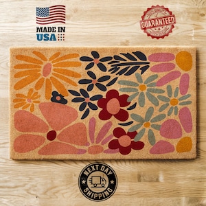 May include: A brown coir doormat with a colorful floral design. The design features pink, red, orange, blue, and green flowers. The doormat has the text "Next Day Shipping" on the bottom.