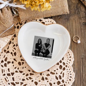 Peut inclure: Un vide-poches blanc en forme de c&oelig;ur avec un bord dor&eacute;, avec une photo en noir et blanc de deux personnes. La photo est centr&eacute;e sur le plat, avec les mots "Always better together" imprim&eacute;s en dessous. Une bague en or avec un diamant est &agrave; proximit&eacute;.