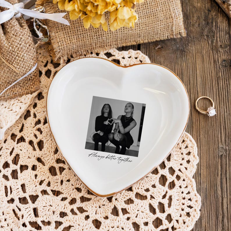 Peut inclure: Un vide-poches blanc en forme de c&oelig;ur avec un bord dor&eacute;, avec une photo en noir et blanc de deux personnes. La photo est centr&eacute;e sur le plat, avec les mots "Always better together" imprim&eacute;s en dessous. Une bague en or avec un diamant est &agrave; proximit&eacute;.