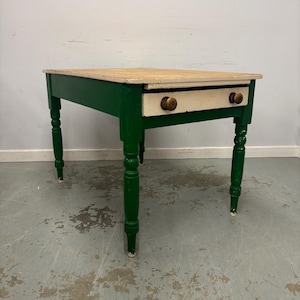 May include: An antique table in green and cream, featuring a single drawer. The table has a natural wood top and turned legs. The drawer has two wooden knobs. The table is approximately 76 cm long, 51 cm wide, and 76 cm high.