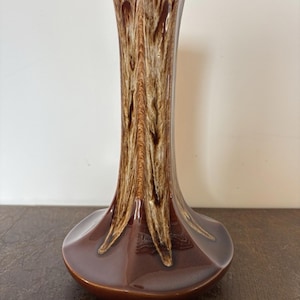 Puede incluir: Un jarrón de cerámica marrón con un diseño único. El jarrón tiene una base acampanada y un cuello alto y esbelto. El exterior presenta un patrón texturizado en tonos marrones y crema, creando un efecto visual llamativo. El jarrón es adecuado para la decoración del hogar.