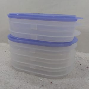 Puede incluir: Un juego de cuatro recipientes de plástico transparente con una tapa azul claro. Los recipientes están apilados uno encima del otro.