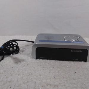 May include: A silver and black digital clock radio with a blue display and the text "Insignia by Best Buy" and "Research Plus" on the front.