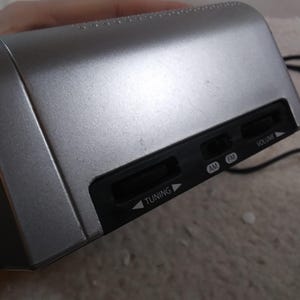 May include: A silver-coloured radio with black buttons labelled "Tuning", "AM", "FM", and "Volume".