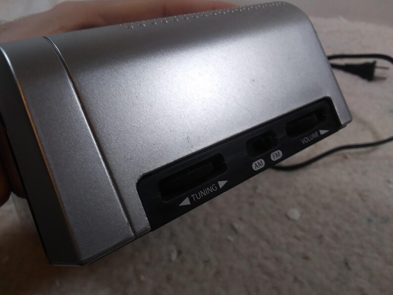 May include: A silver-coloured radio with black buttons labelled "Tuning", "AM", "FM", and "Volume".
