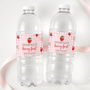 以下が含まれることがあります： ラベルが付いた透明なプラスチック製のウォーターボトルが2本。ラベルにはピンクのギンガムチェック柄とイチゴのデザインが施されています。ラベルのテキストは「SHARENA'S berry first BIRTHDAY MARCH 12, 2025」と書かれています。