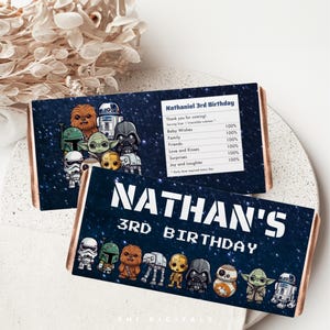 Puede incluir: Dos envoltorios de barras de chocolate con temática de Star Wars. Uno dice "Nathaniel 3rd Birthday" y el otro "Nathan's 3rd Birthday". Ambos envoltorios presentan personajes de Star Wars y un fondo estrellado.
