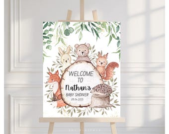 May include: A watercolor baby shower welcome sign featuring woodland animals: a fox, rabbit, bear, squirrel, and hedgehog. The sign reads "Welcome to Nathan's Baby Shower 08.04.2025" on a wood slice, surrounded by greenery.