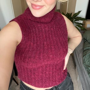 Könnte beinhalten: Ein burgunderfarbener ärmelloser Rollkragenpullover mit gerippter Strickstruktur.