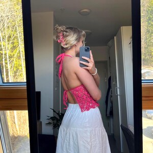 May include: A pink crochet halter top with a white skirt. The top has a low back and is tied at the neck.