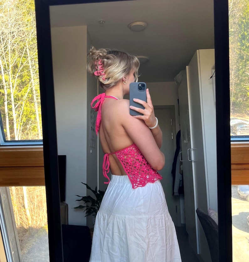 May include: A pink crochet halter top with a white skirt. The top has a low back and is tied at the neck.