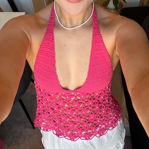 May include: A pink crocheted halter top with white beads. The top has a scalloped hem and a deep V-neckline.