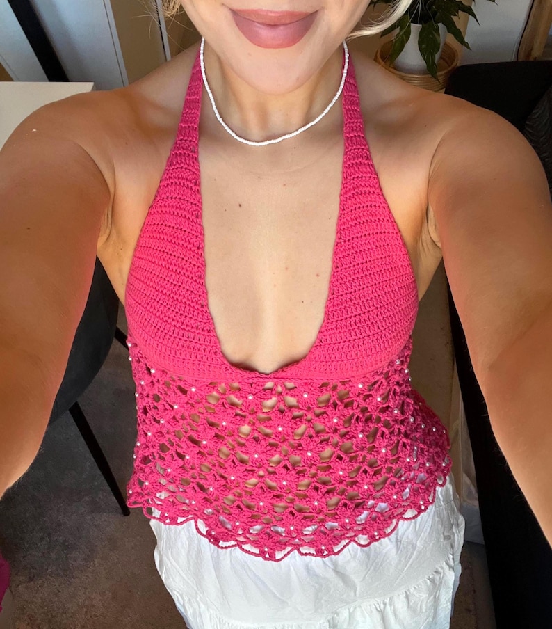 May include: A pink crocheted halter top with white beads. The top has a scalloped hem and a deep V-neckline.