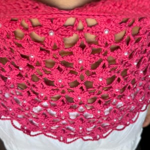 May include: A pink crocheted top with a floral design and white beads.
