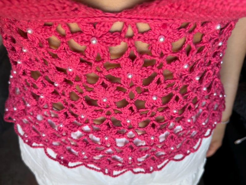 May include: A pink crocheted top with a floral design and white beads.
