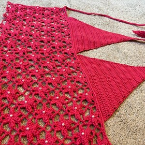May include: A red crocheted halter top with a delicate floral pattern and white beads. The top has a V-shaped neckline and adjustable straps.