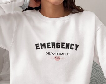 May include: White sweatshirt featuring the text "EMERGENCY DEPARTMENT" in black. Below, the name "Julia" is written in cursive, accompanied by a pink heartbeat line and circle.