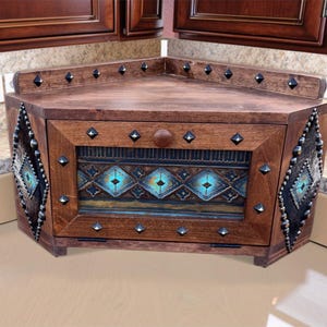 May include: A wooden corner cabinet with a dark brown finish. The cabinet features decorative metal studs and a central panel with a turquoise and brown geometric design. The cabinet is designed to fit into a corner space.